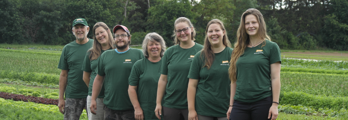 KI generiert: Eine Gruppe von Menschen in grünen T-Shirts posiert vor einem landwirtschaftlichen Hintergrund.