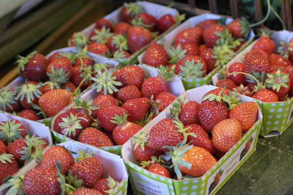 KI generiert: Frische Erdbeeren in grünen Pappschalen auf einem Marktstand.