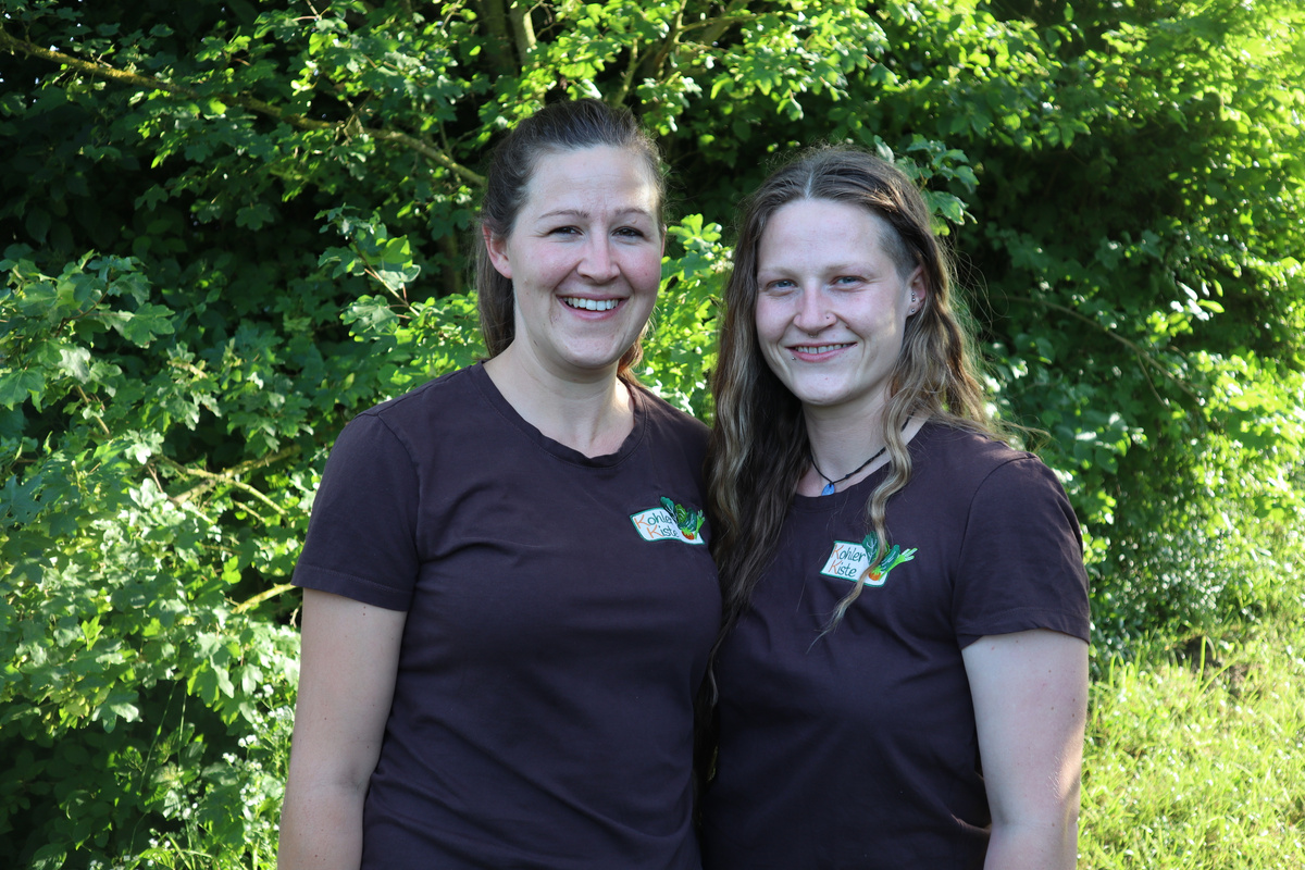 KI generiert: Zwei Personen lächeln in die Kamera, vor einem Hintergrund aus grünen Bäumen.